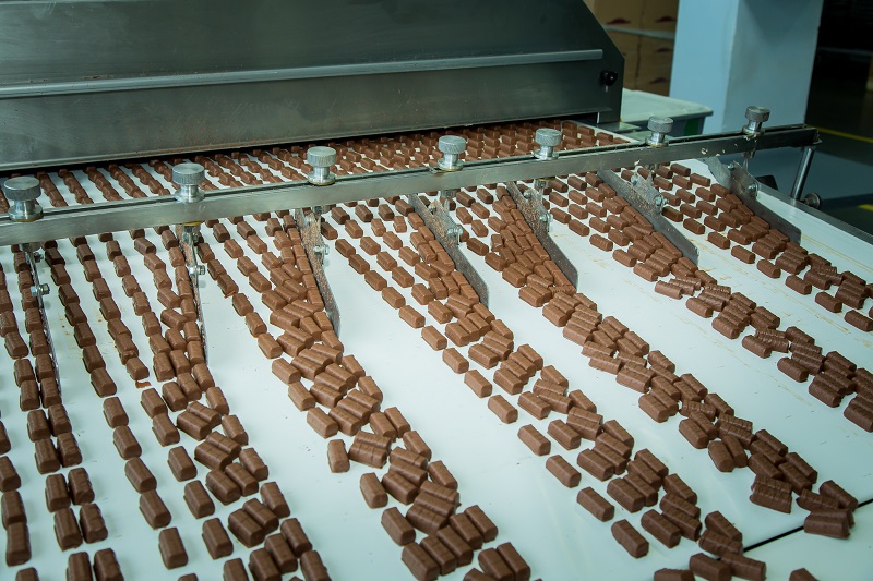 Widok na taśmę produkcyjną w fabryce słodyczy. Na taśmie czekoladowe cukierki